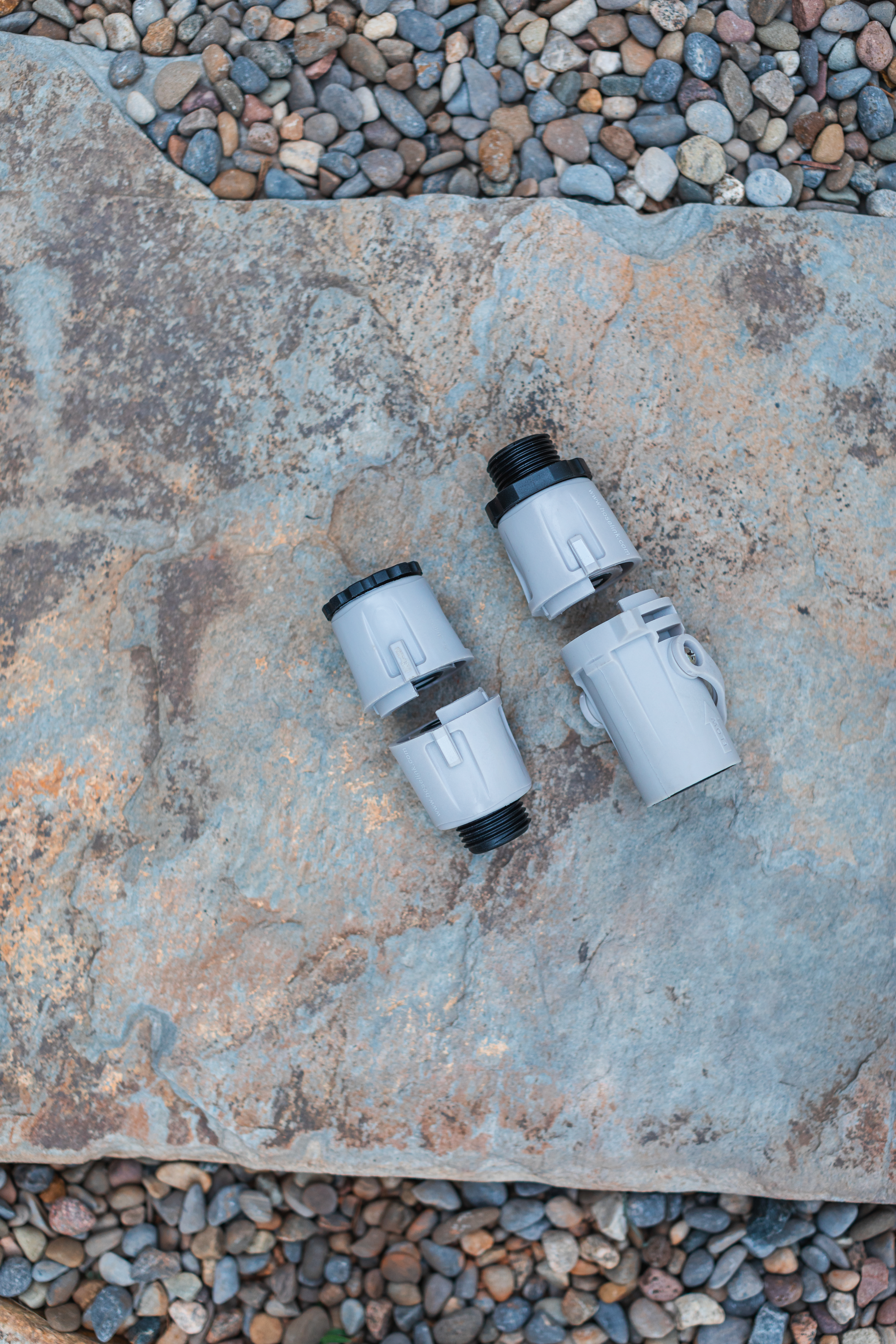 Two Hoselink fittings on a stone surface with gravel.