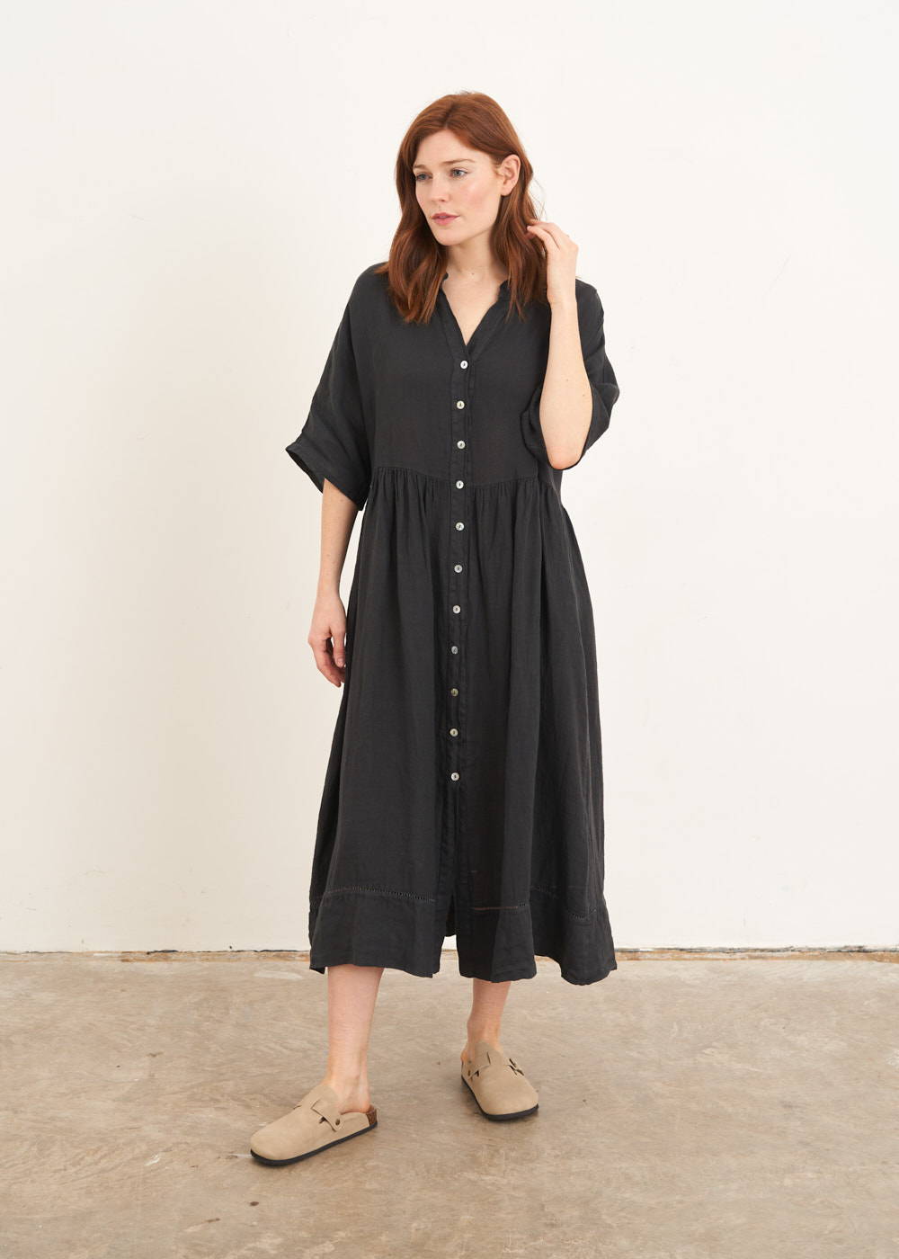 A model wearing an oversized linen midi shirt dress in dark grey with mother of pearl buttons 