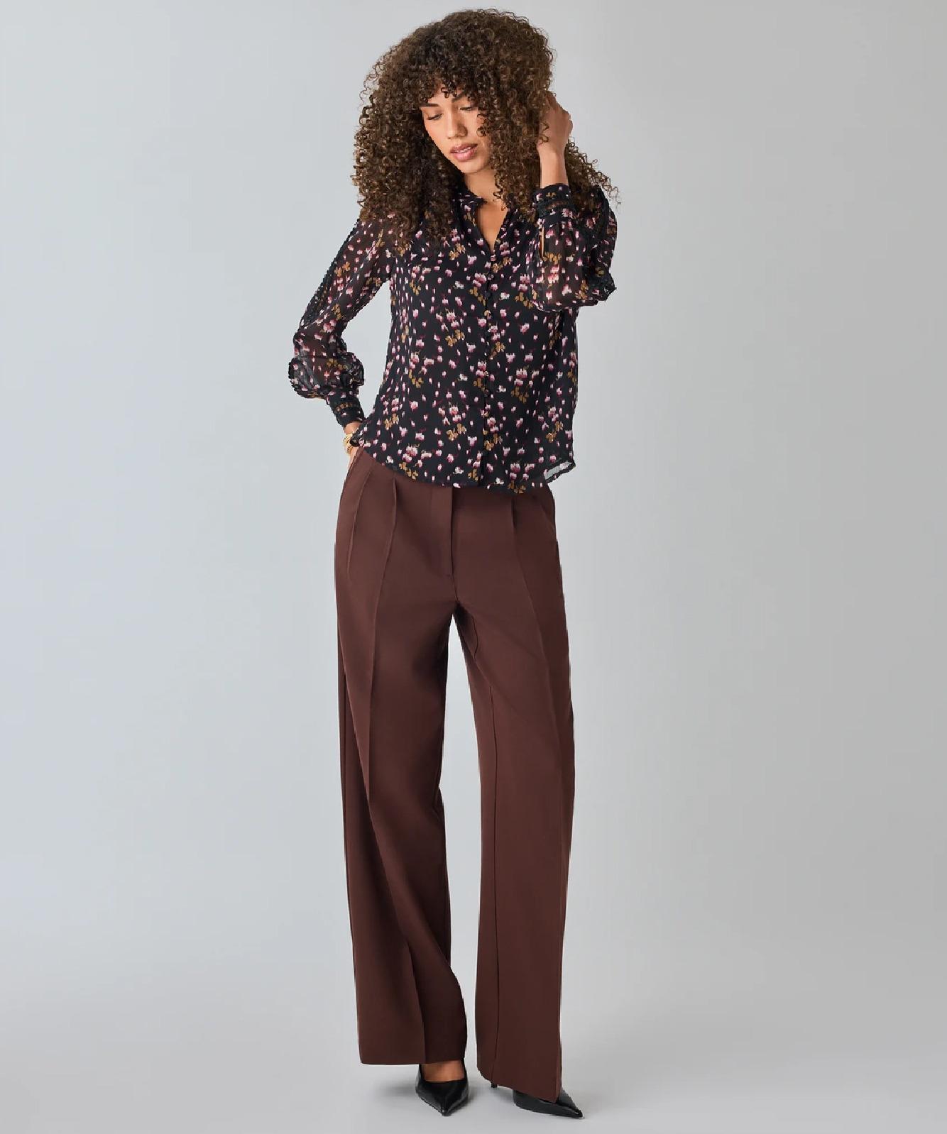 Model wearing a floral blouse and wide-legged brown trousers.
