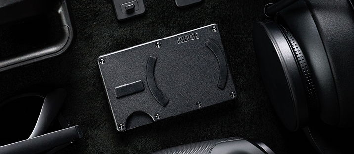 A sleek black wallet among various accessories on a dark surface.