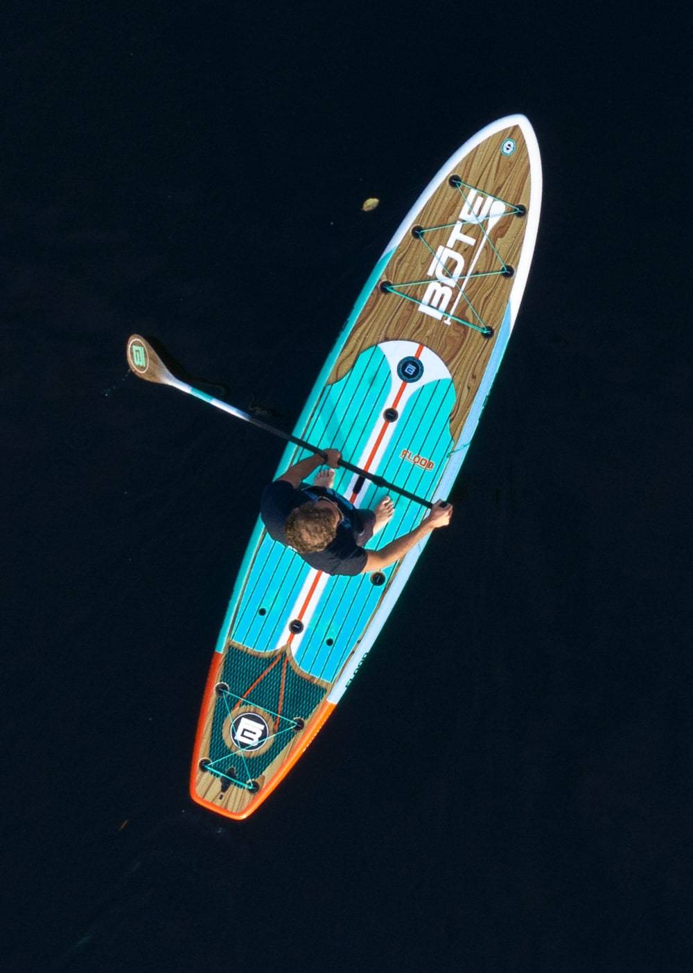 Overhead view of a man paddling the Flood 10′6″ Classic Teak Paddle Board