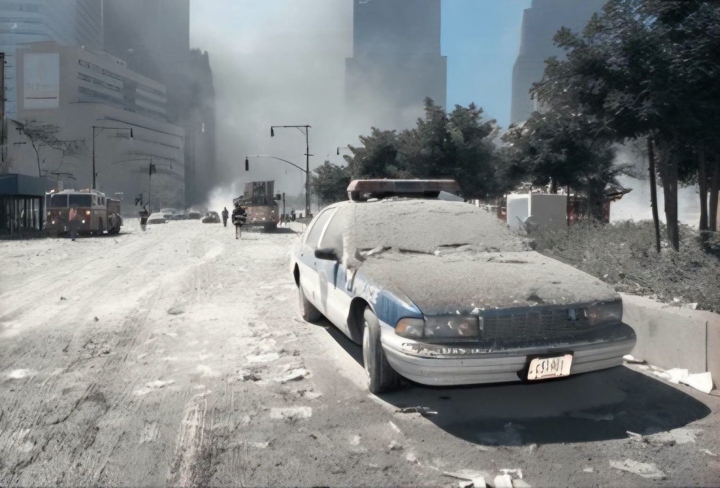 A dusty police car on a deserted street with buildings in the background.