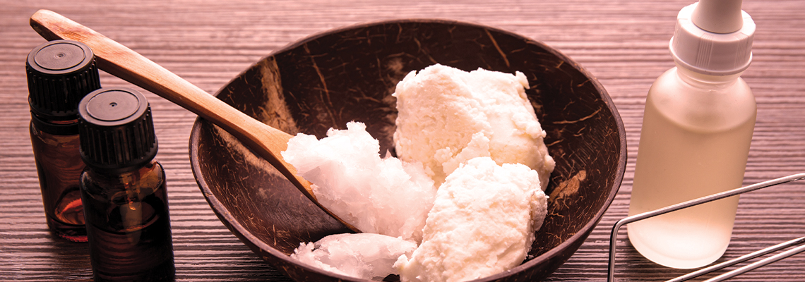 Bowl of cream with wooden spoon, essential oils, and a glass bottle.