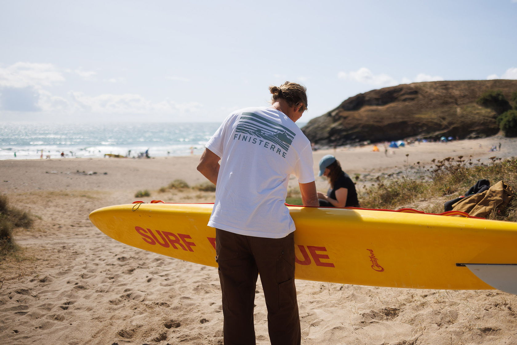 Lifeguard assisting a person with a surfboard on the beach.