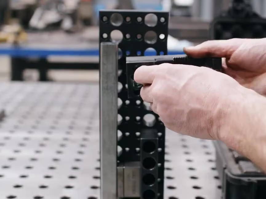 Person adjusting a black metal fixture on a worktable in a workshop.