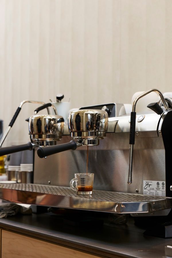 Coffee machine with two portafilters and a measuring cup on the counter.