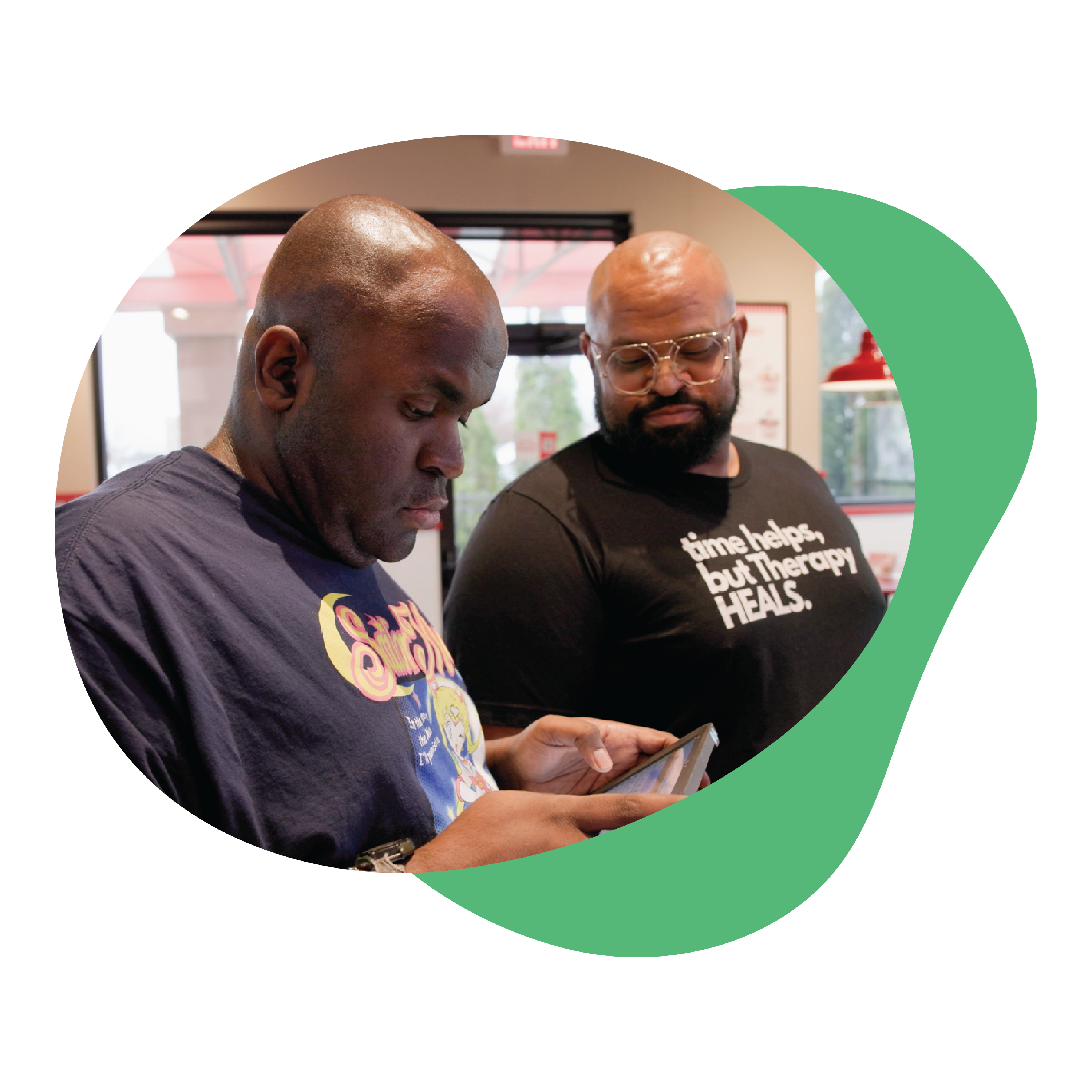 Two men interacting in a casual setting, one looking at an AAC device.