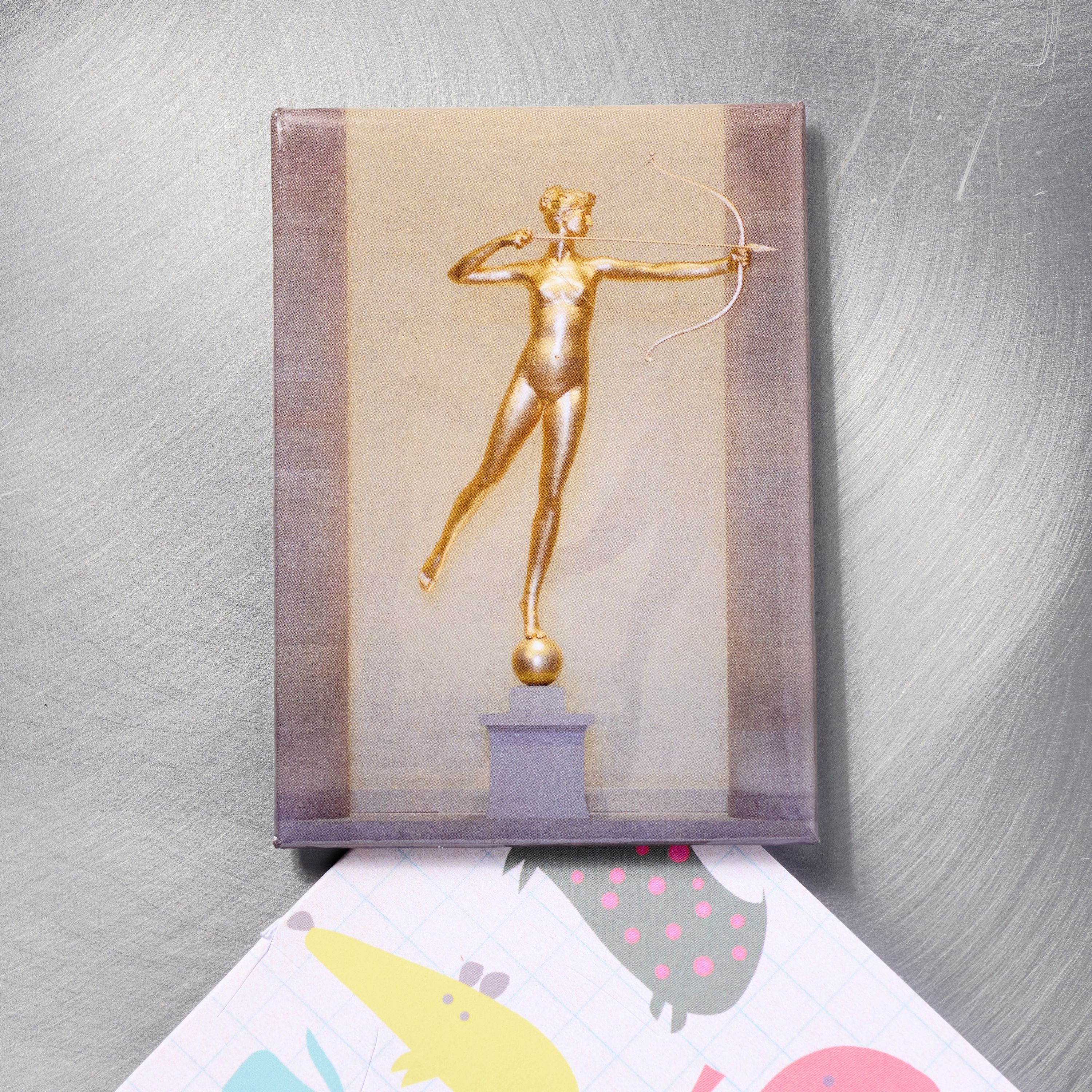 Magnet featuring a golden statue of an archer on a metallic surface.