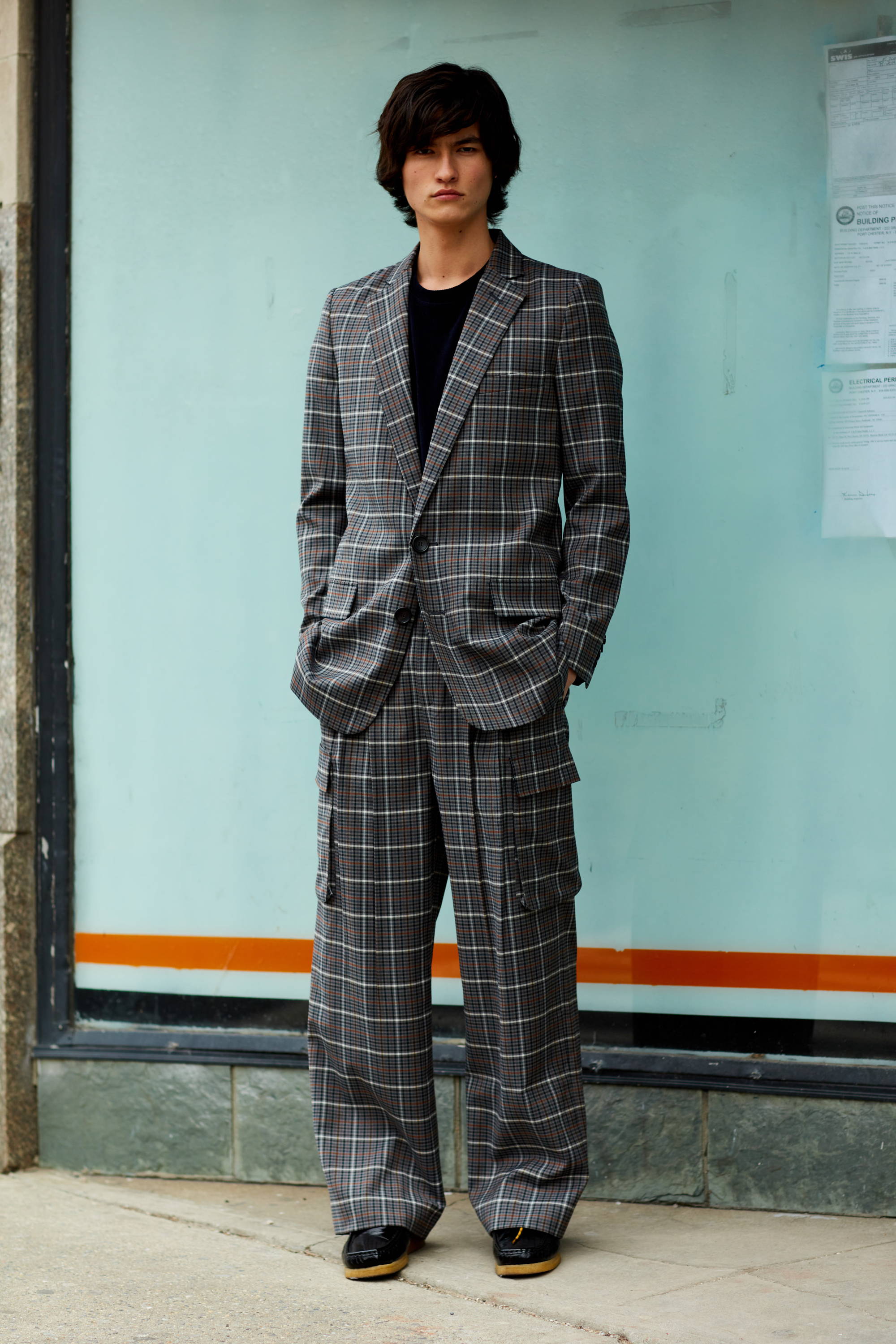Young man in a plaid suit standing against a glass wall.
