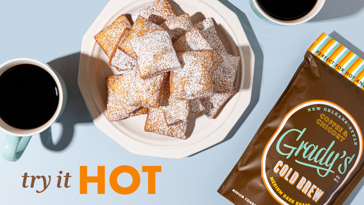 Hot coffee beside powdered beignets and a Grady's Cold Brew Bean Bag package with the words try it hot.