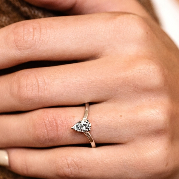 a delicate gold solitaire wedding ring with a pear shaped lab diamond