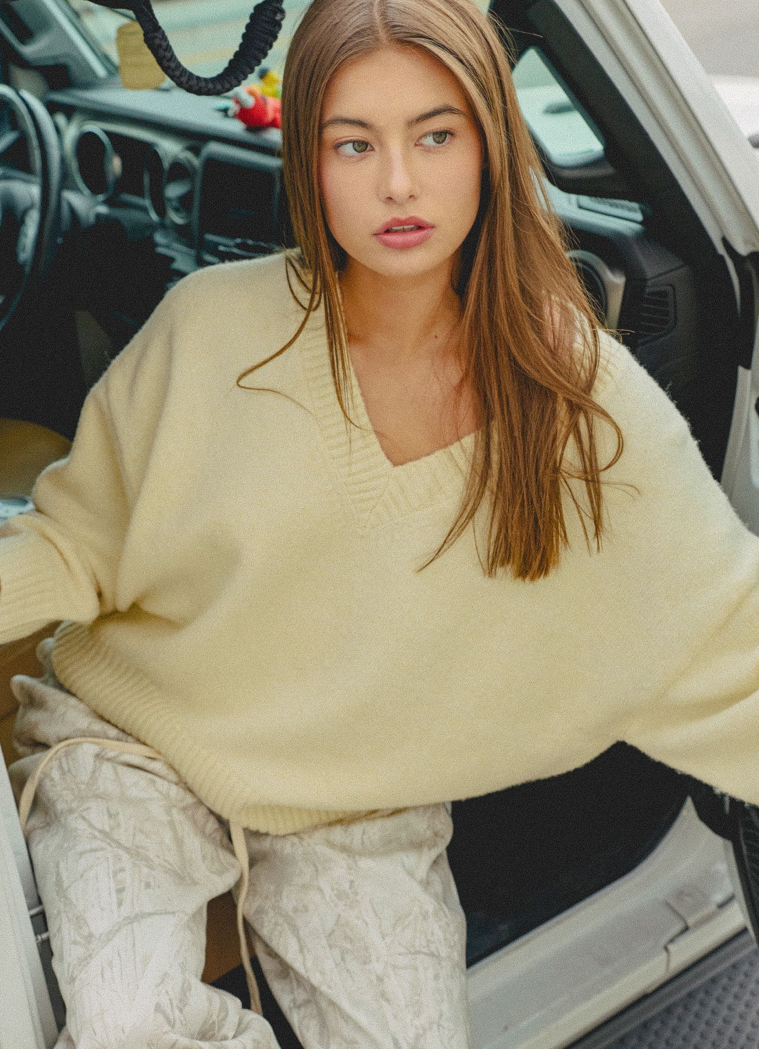Young woman in oversized sweater sitting in a car doorway.