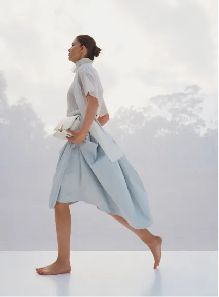 A woman walks barefoot in a light blue outfit against a soft background.