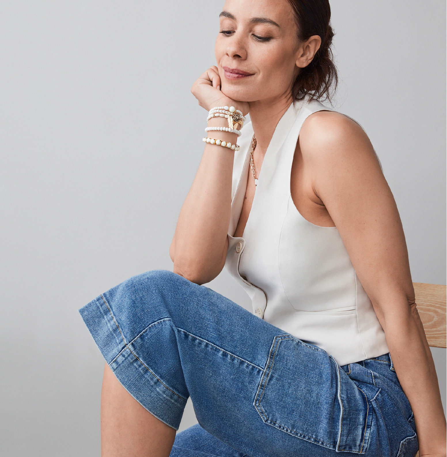 A woman in a sleeveless top sits thoughtfully, wearing denim shorts.
