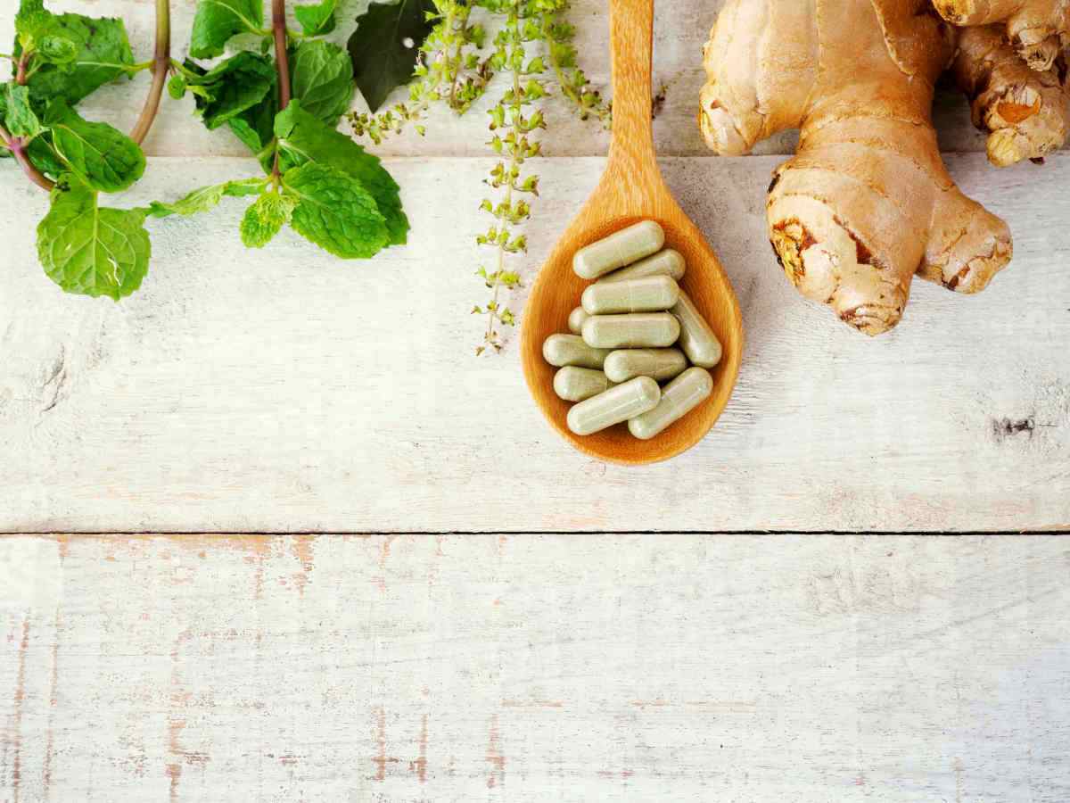 Herbal pills on wooden spoon with ginger root and green plant | Surprising Differences of Whole Food Vitamins Vs. Synthetic Vitamins | organic vitamins vs regular vitamins