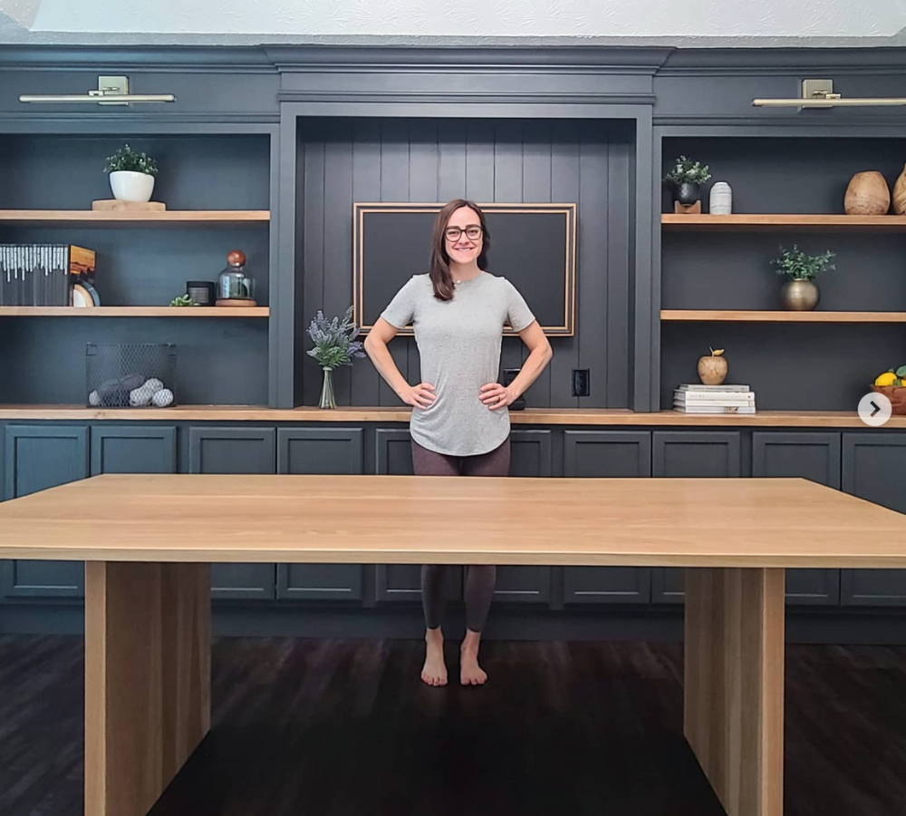 woman standing in her custom built kitchen in front of a blue wooden pantry and large live oak wood table coated in high gloss table top epoxy