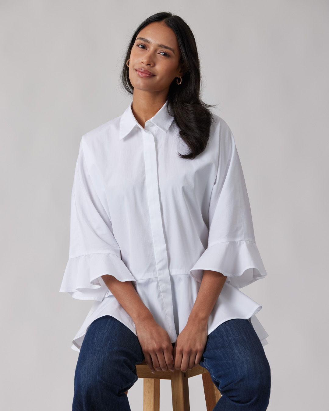 Woman sitting on a stool, wearing a white shirt and blue jeans.