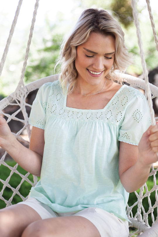 Woman sitting on swinging chair outside on porch wearing Seychelle Top in light green color.