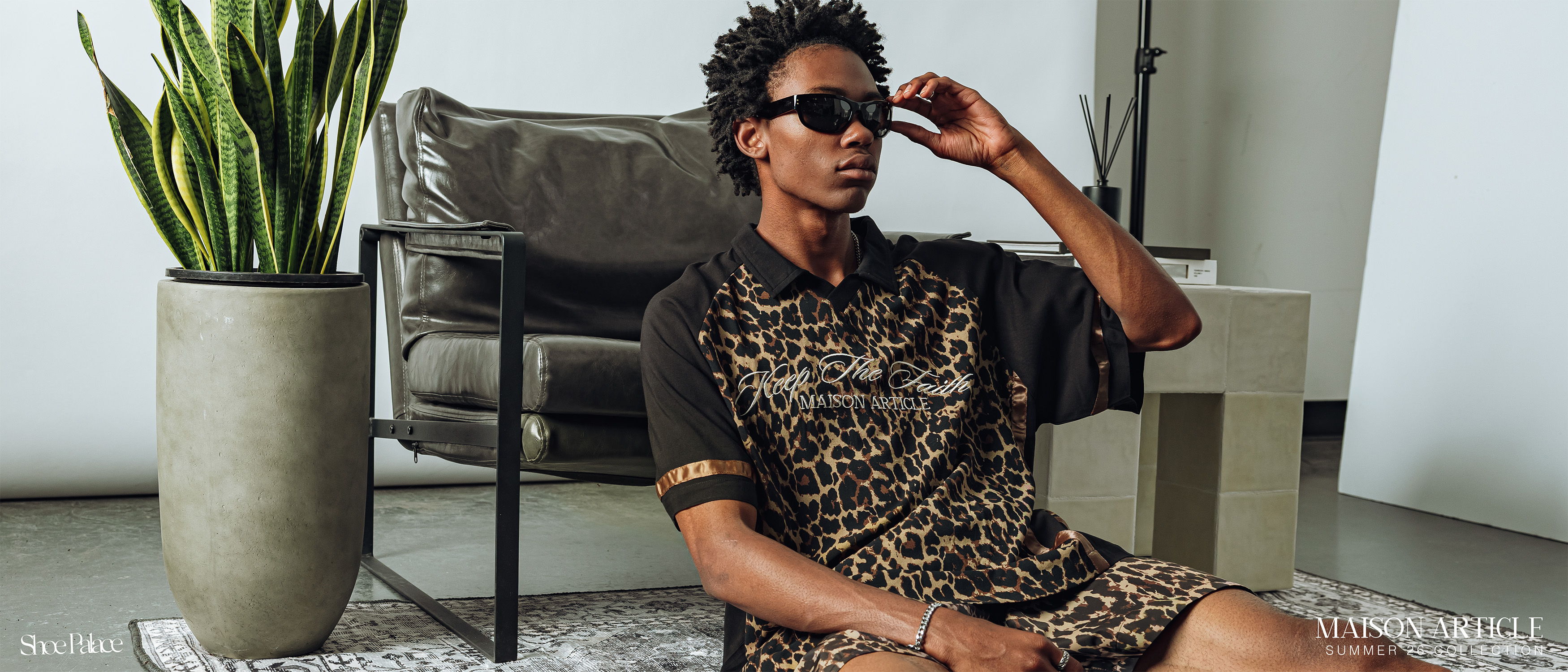 Person wearing sunglasses, sitting on a rug beside a plant in modern decor.