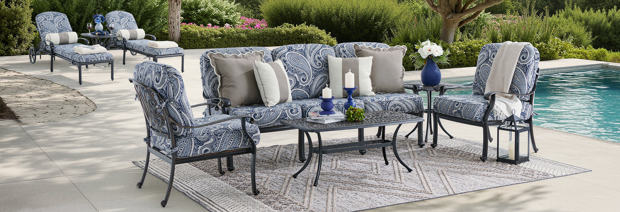 Outdoor seating area by a pool with decorative cushions and a table.