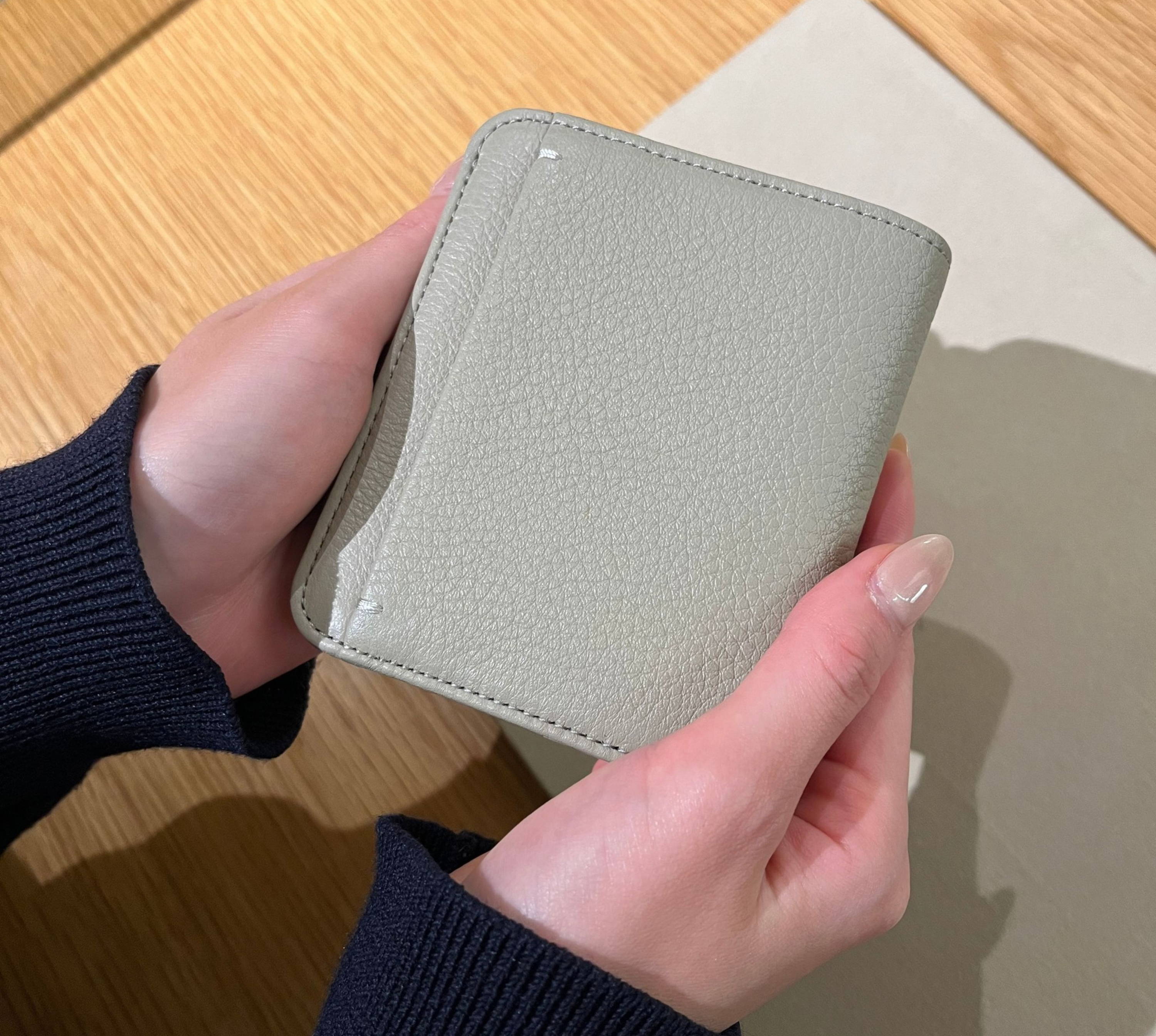 A person holding a light gray wallet on a wooden surface.