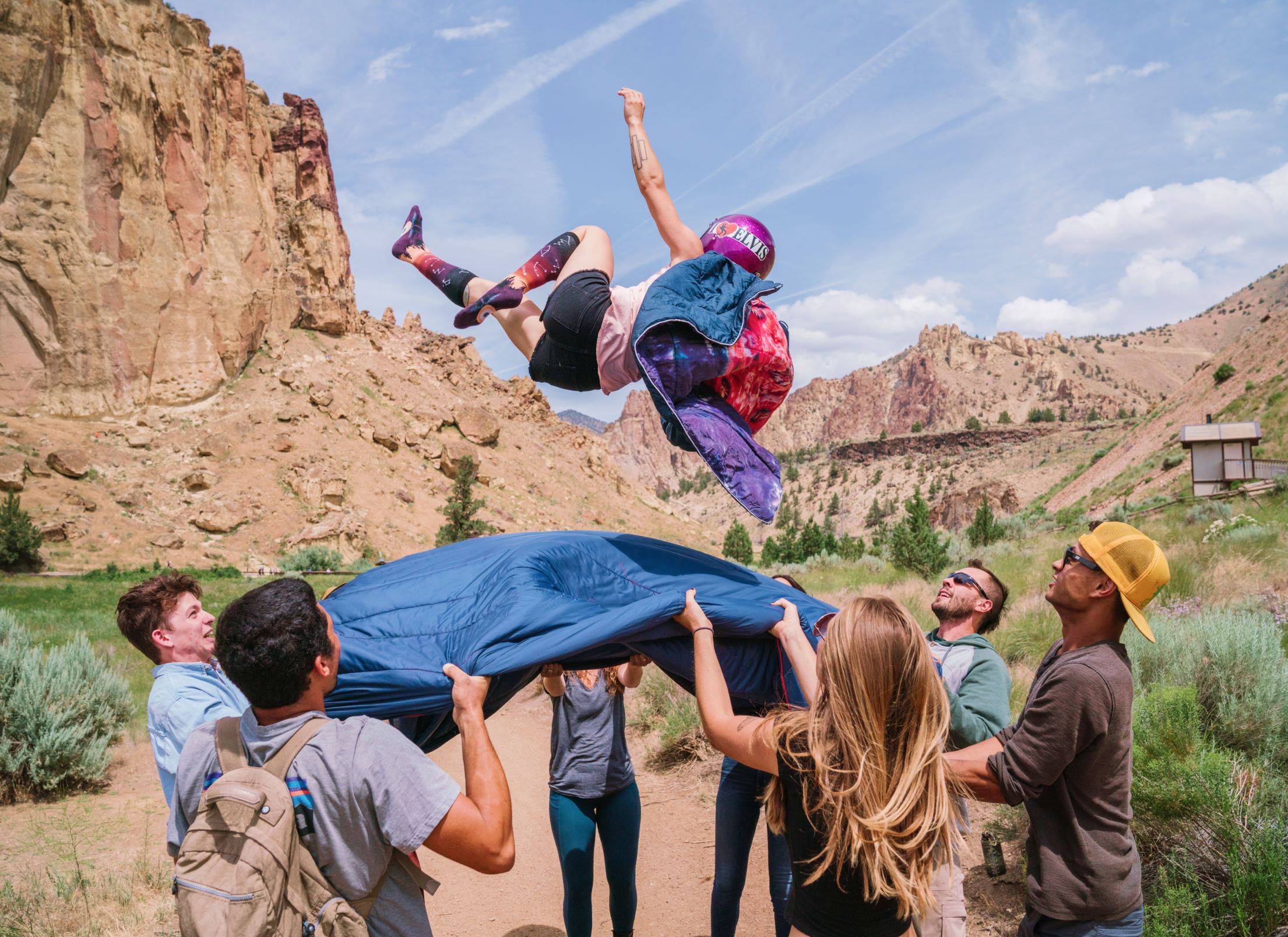 A person suspended mid-air, propelled by laughter and the warmth of friendship, as they're playfully tossed by a group using a cozy Rumpl blanket.
