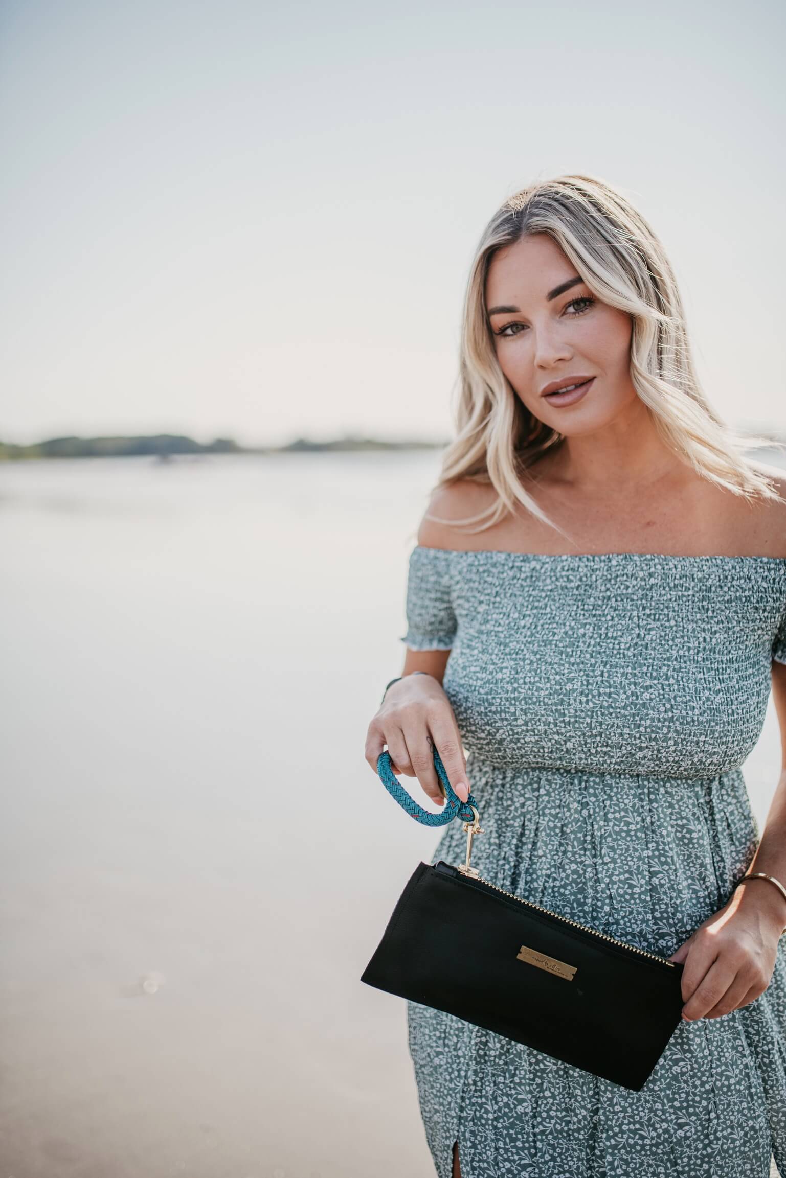 woman holding black leather clutch with teal strap on the beach