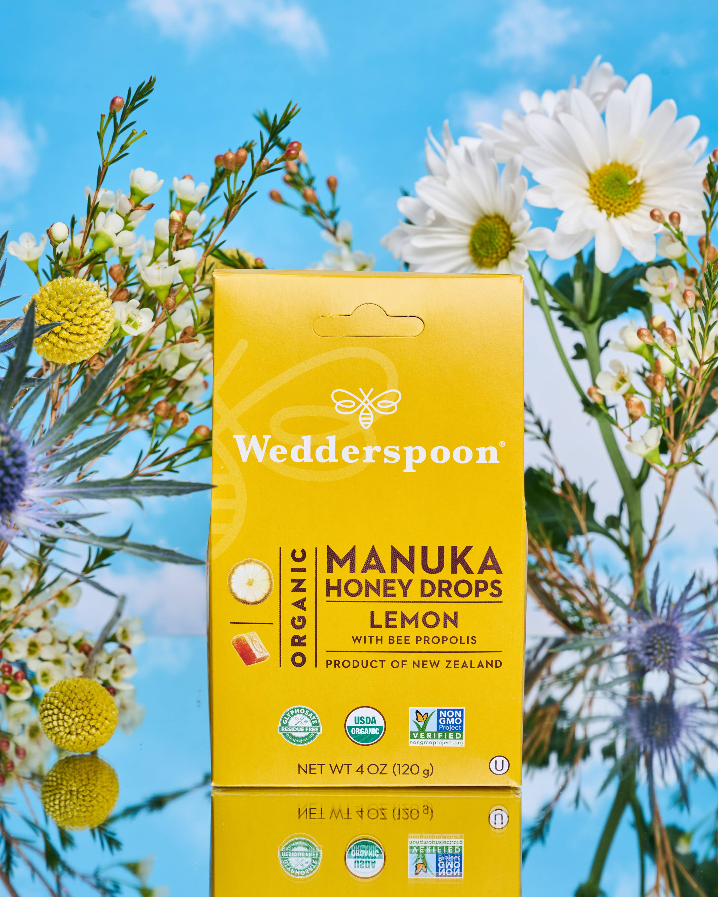 Box of lemon Manuka honey Drops in front of Pollinator friendly flowers
