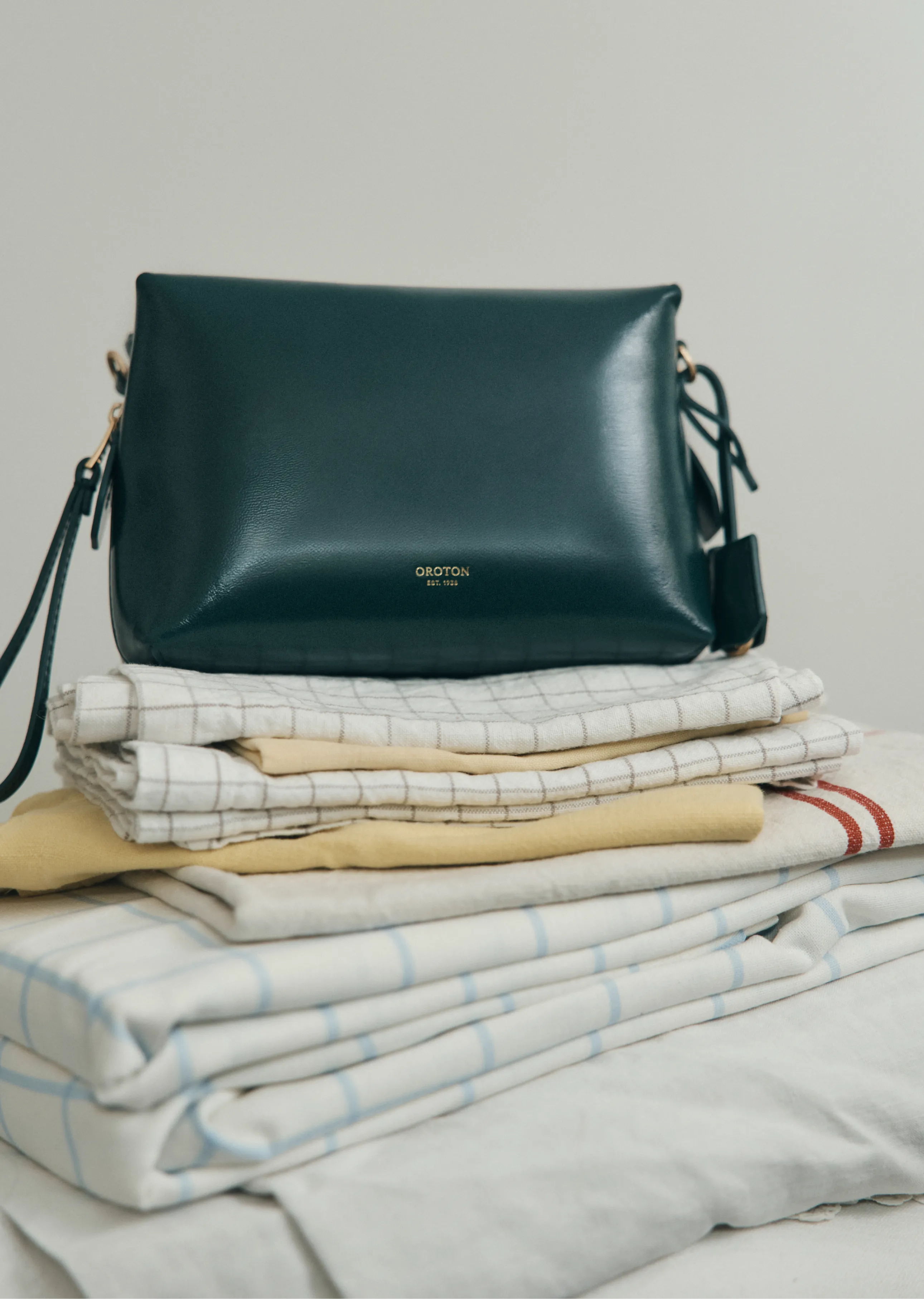 A green leather bag on a stack of folded blankets.