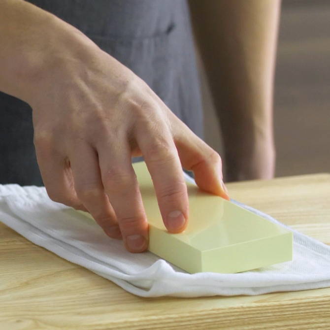 A chef placing a wet 6000-grit Misen Sharpening stone onto a kitchen towel on a wood countertop.