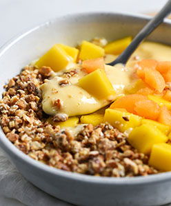 Bowl of granola topped with mango and creamy sauce.