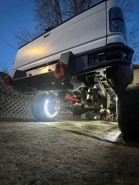 Rear undercarriage of white lifted Ram with LED wheel ring light and aftermarket bumper at dusk