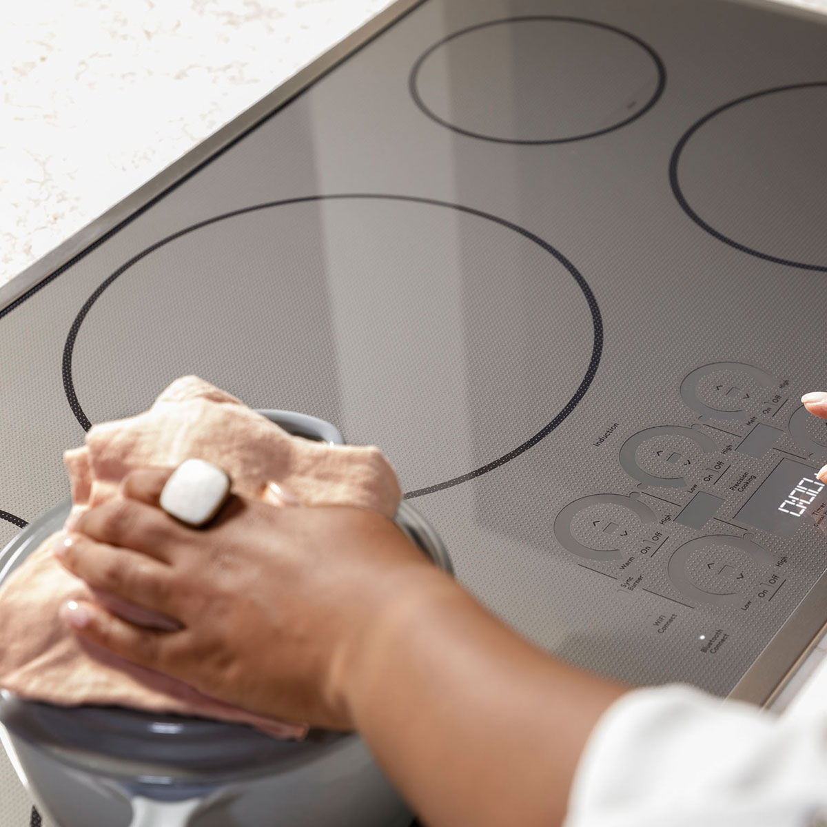 A person wiping a modern induction cooktop with a cloth.