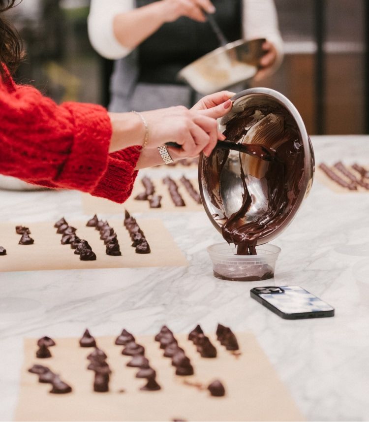 Person pouring chocolate onto parchment paper with another person in the background.