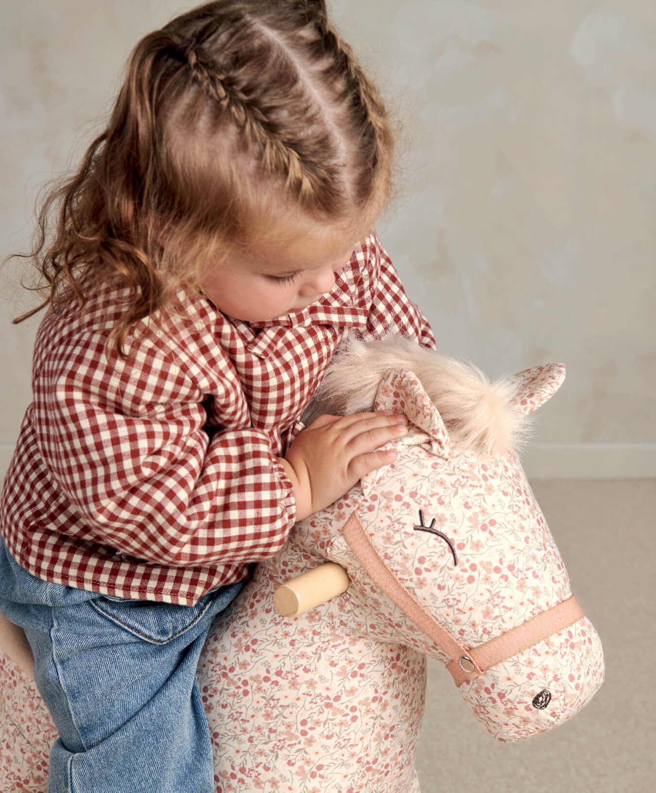 Child playing with a stuffed horse toy, wearing a checkered shirt.