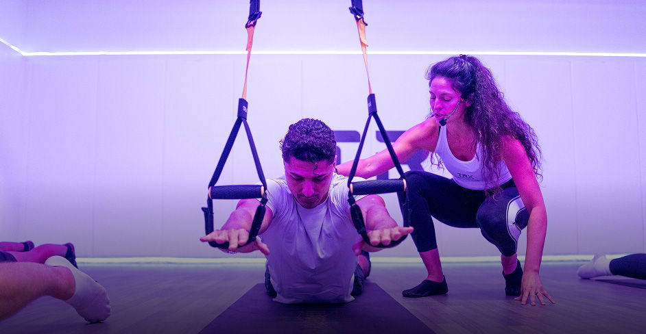 Person exercising with TRX straps while being assisted by another individual.