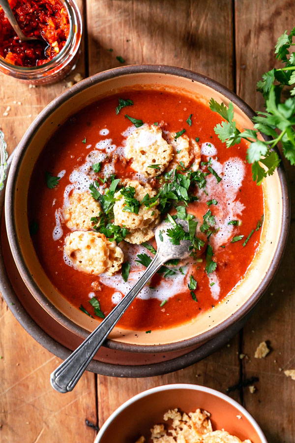 A spcy tomato soup topped with parsley and crispy parmesan coins.