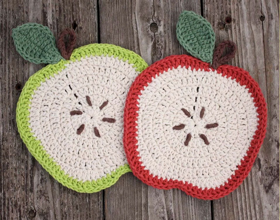 Crocheted apple coasters in green and red on a wooden background.