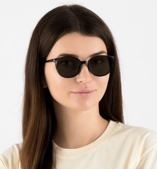 woman with soft square face wearing Serene Black, oval frame sunglasses, on a white background