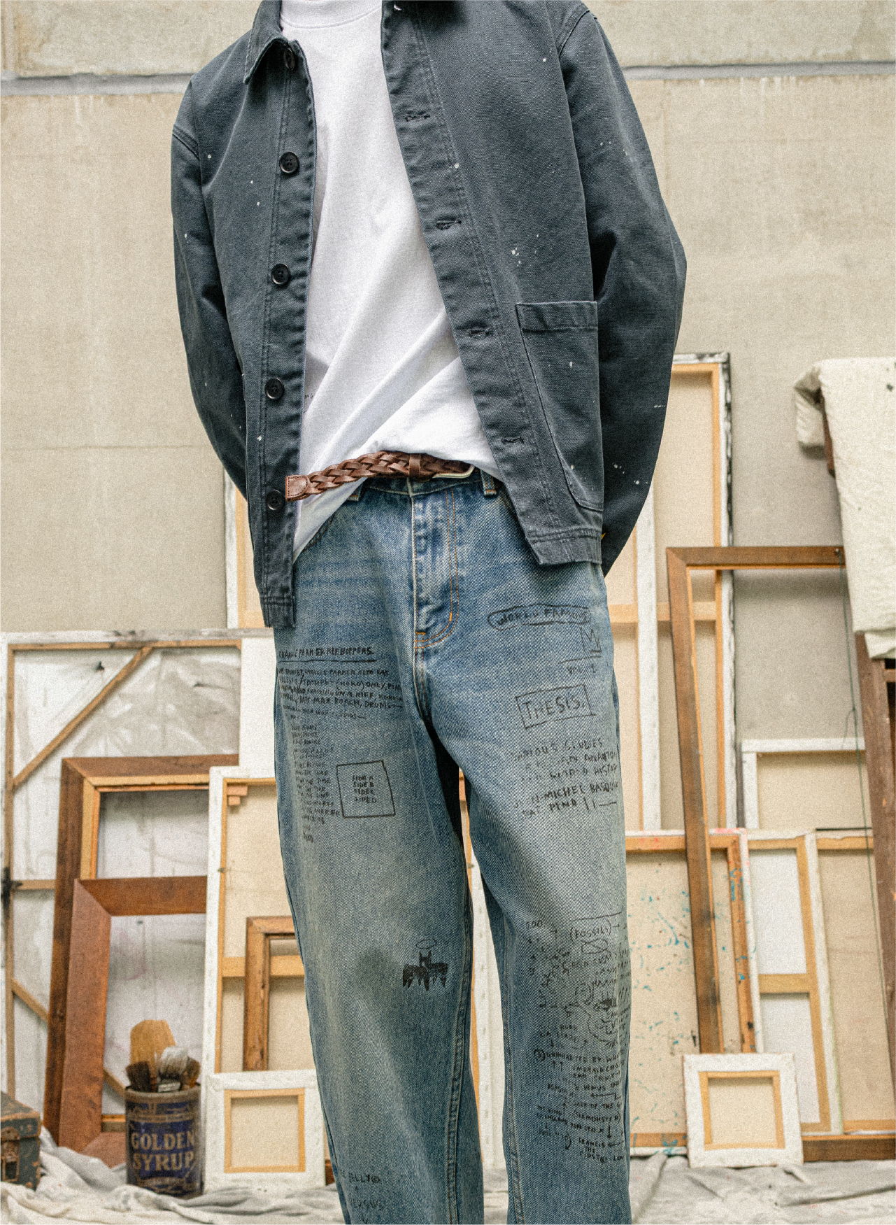 Person wearing a gray jacket and blue jeans, standing in front of frames.