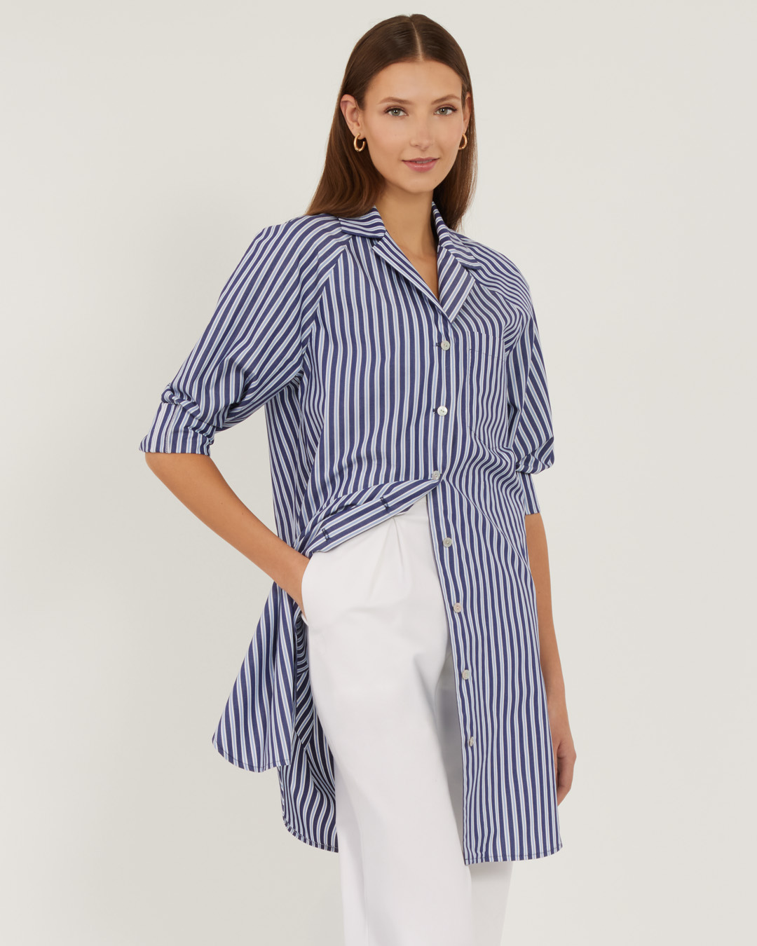 Woman in a striped shirt and white pants, posing confidently.