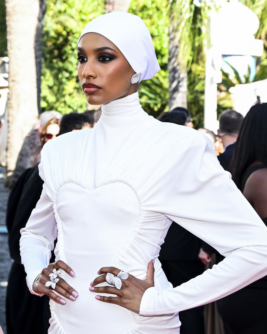 A woman in a white dress poses at Cannes Film Festival wearing Pasquale Bruni jewels: Aleluia earrings and Giardini Segreti rings.