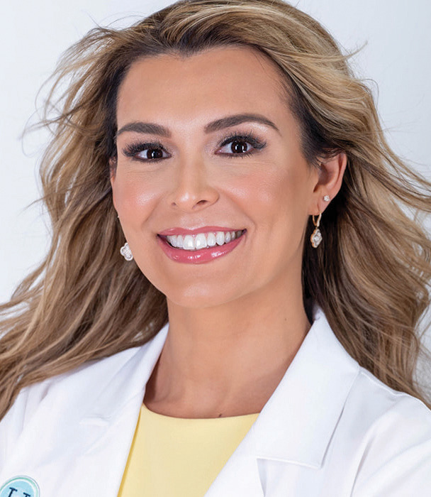 Smiling woman in a white coat with earrings and wavy hair.
