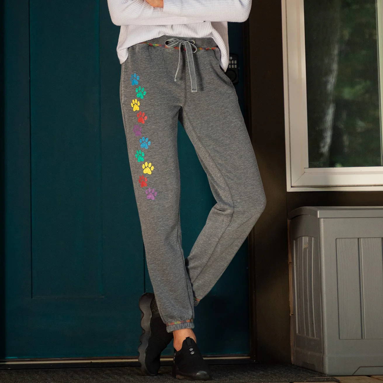 Woman standing in front of a blue door with a colorful paw print design on gray pants.