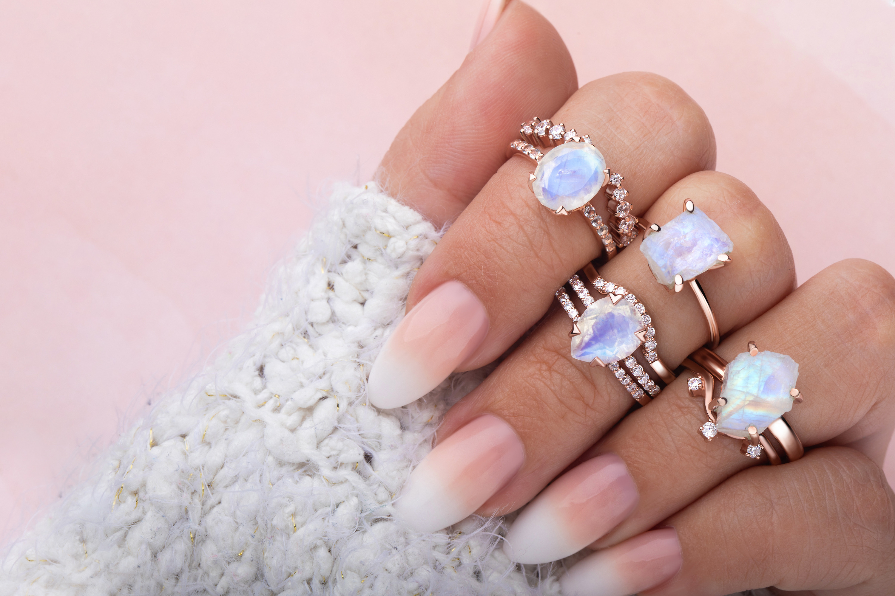 Four Moonstone rings combined with band rings in different styles are shown on a hand.