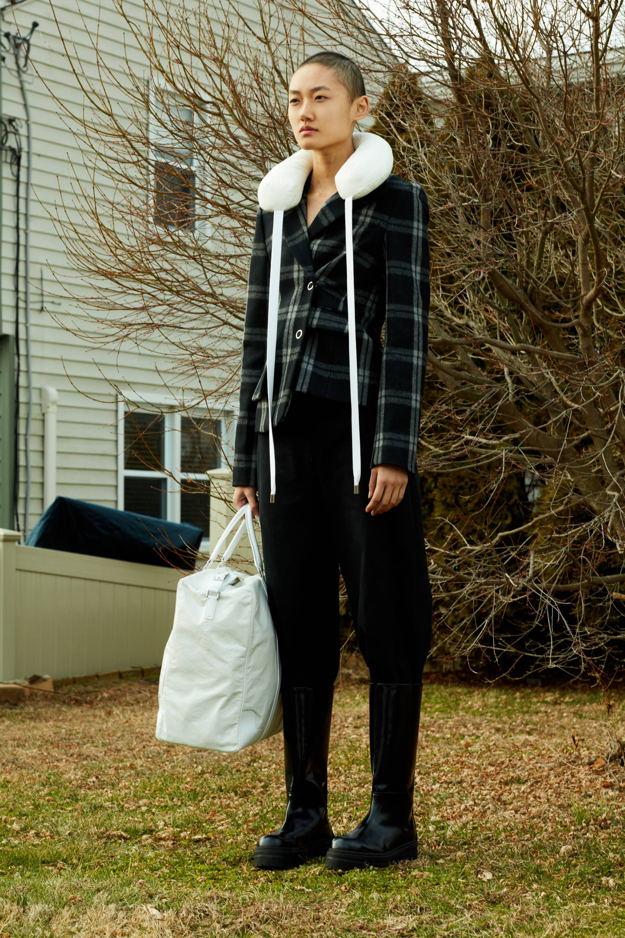 Person standing outdoors in a stylish outfit with a white bag.