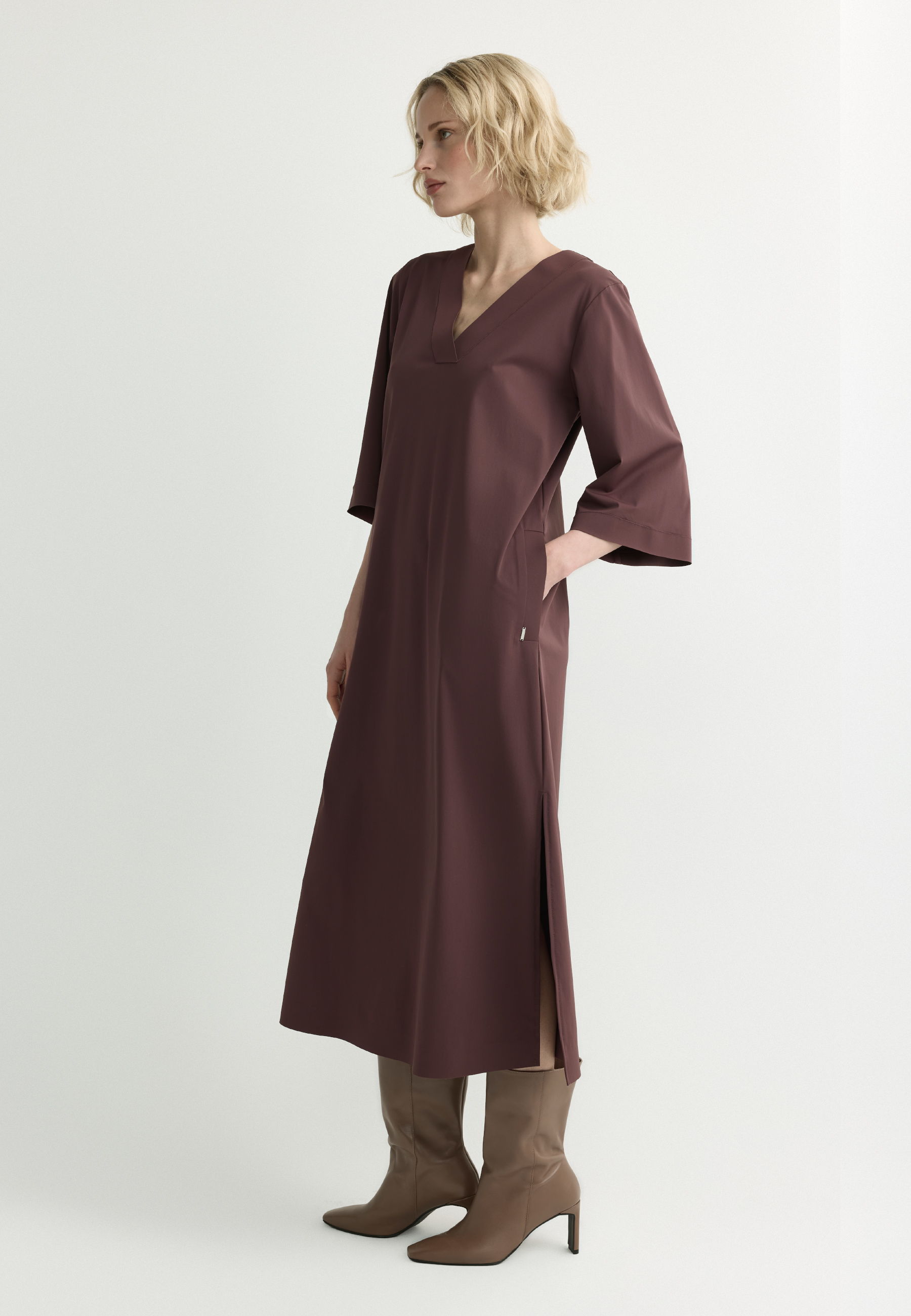 A model wearing a long, burgundy dress and knee-high brown boots.