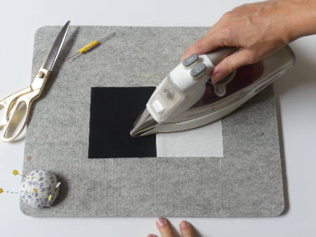 a hand holding a hot iron pressing a quilt block on a wool pressing mat