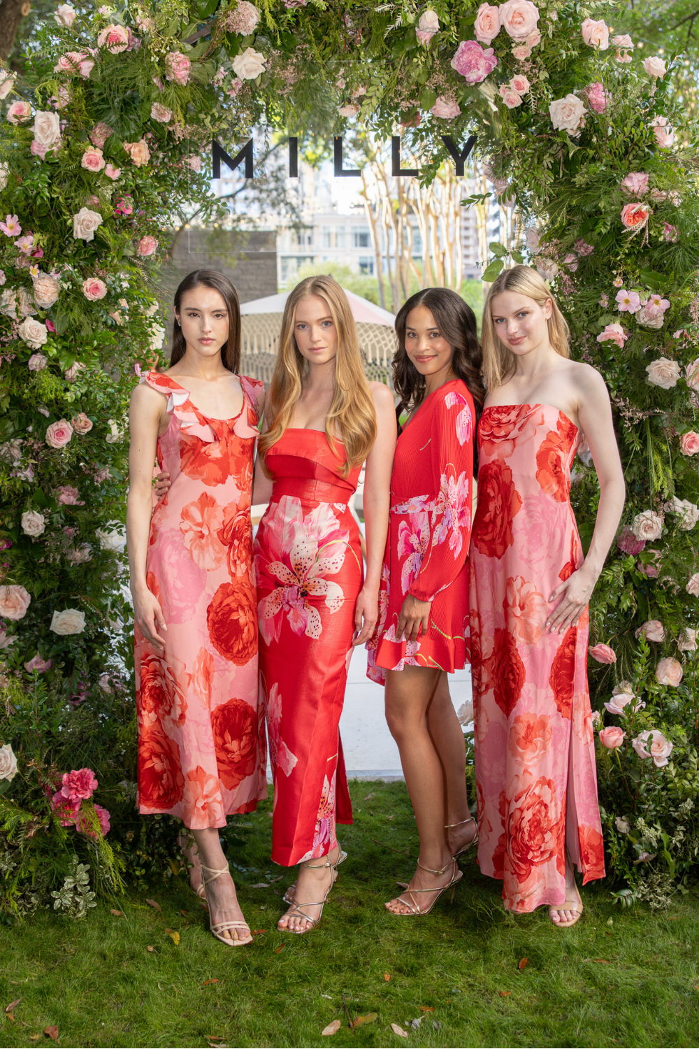 Four models wearing floral dresses pose in a garden setting.