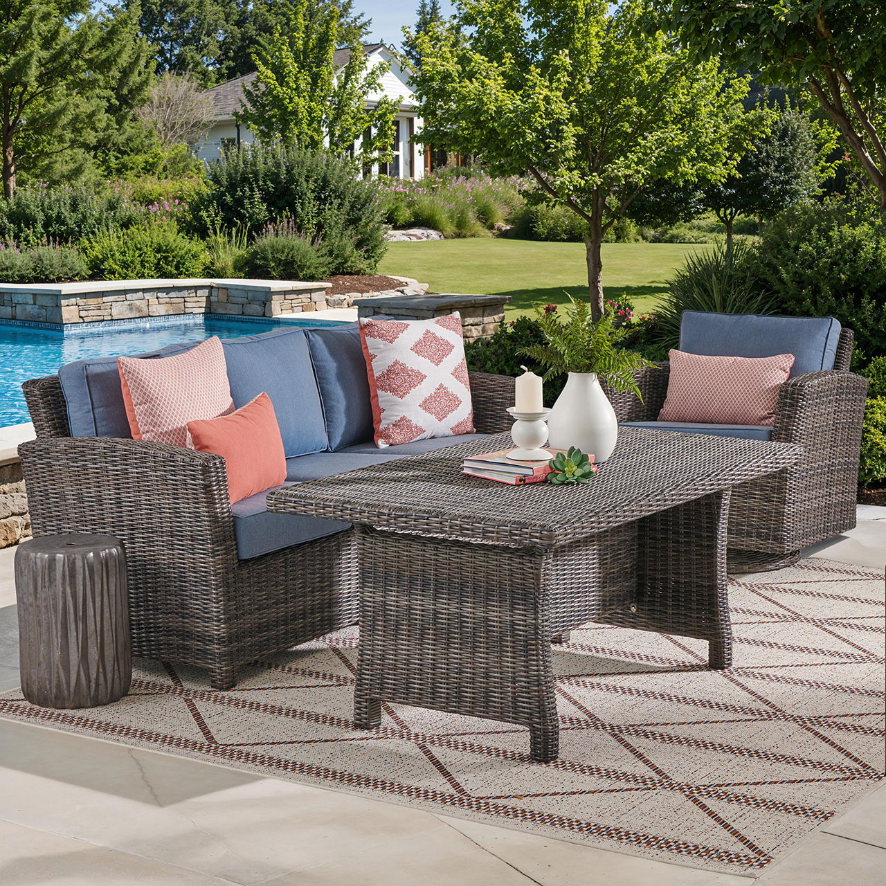 Outdoor seating area with wicker furniture, cushions, and a table by a pool.